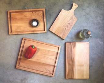 May include: Four wooden cutting boards of different sizes and shapes. One board has a small bowl with white powder on it. Another board has a red bell pepper on it. The boards are on a gray concrete surface.