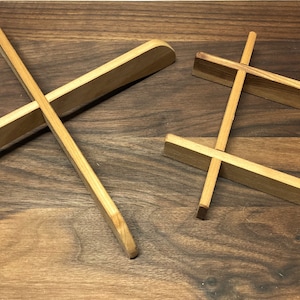 May include: Two wooden coasters, one in a cross shape and the other in a square shape with a grid pattern. Both coasters are made of light brown wood.