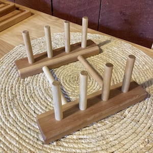 May include: Wooden plate rack with six dowels for holding plates upright. The rack is made of natural wood and has a rustic look.