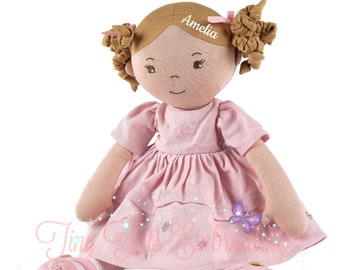May include: A pink and brown fabric doll with brown hair in pigtails. The doll is wearing a pink dress with embroidered flowers and a butterfly. The doll's name, "Amelia", is embroidered on the doll's forehead.