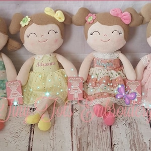 May include: Four plush dolls with embroidered faces and dresses. Each doll has a different name embroidered on their dress: Kamryn, Adrienne, Harper, and Annie.