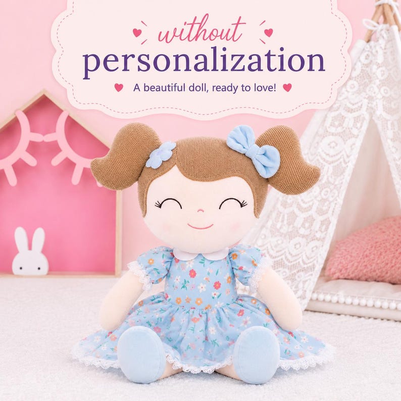 May include: A plush doll with brown yarn hair styled in pigtails, featuring a light blue bow and flower accessory. The doll wears a light blue dress with a floral pattern, white lace trim, and a white collar. Text reads: without personalization.