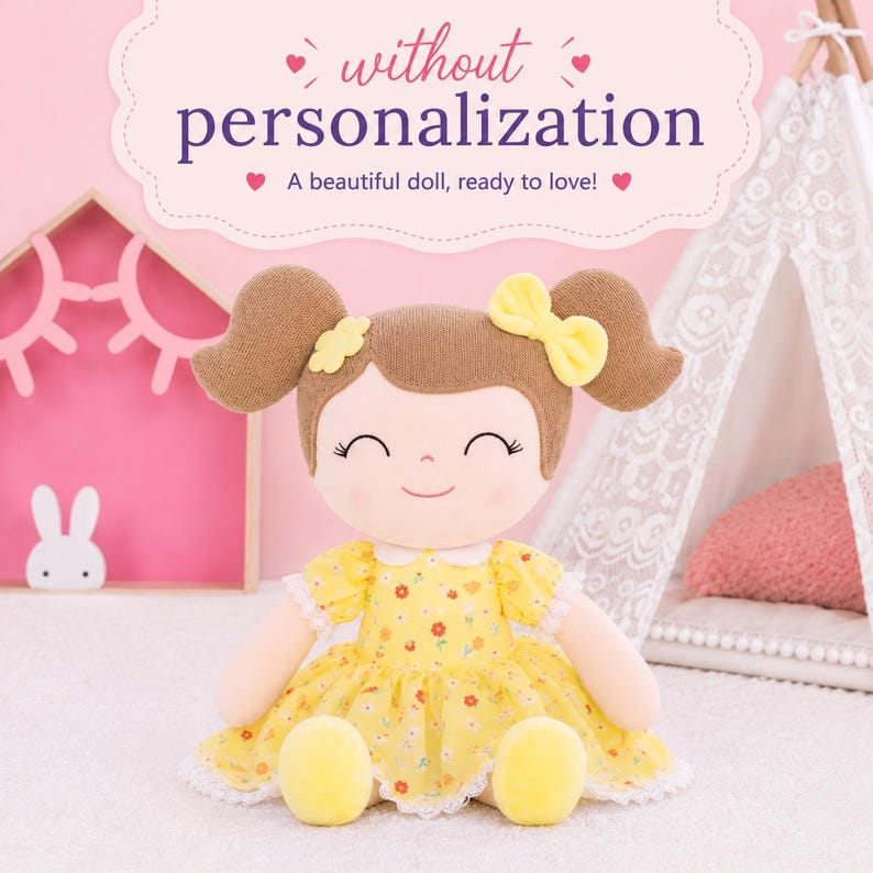 May include: A plush doll with brown hair in pigtails, wearing a yellow floral dress with white lace trim and a yellow bow. The text above reads: without personalization. A beautiful doll, ready to love!