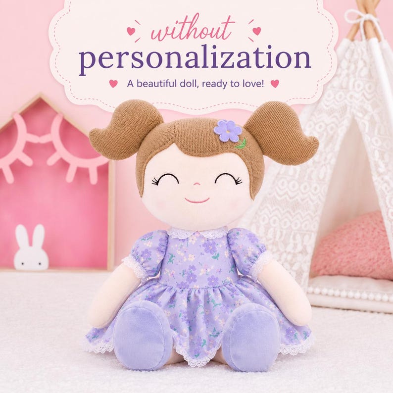 May include: A plush doll with brown hair styled in two pigtails, featuring a small purple flower accessory. The doll wears a light purple dress with a floral pattern and white lace trim. Text above the doll reads: without personalization A beautiful doll, ready to love!