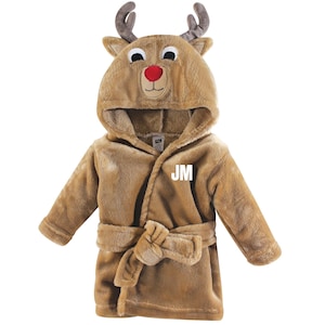 May include: A brown plush reindeer-themed bathrobe with a hood featuring a reindeer face, complete with antlers, eyes, and a red nose. The robe has a belt and the initials "JM" are displayed on the front. This cozy robe is perfect for children.