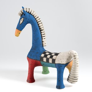 May include: A whimsical ceramic horse sculpture with a blue body, red and green legs, and a checkered pattern on its back. The horse has a white mane and tail, and an orange nose. A unique decorative piece.