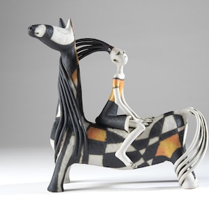 May include: A ceramic sculpture of a stylized horse with a black, white, and orange checkered pattern, featuring a long black mane and a white figure with a gold-accented top sitting on its back, with a white tail and black hooves.