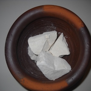May include: White chalk chunks in a brown ceramic bowl. The bowl has a dark brown rim and a lighter brown base.