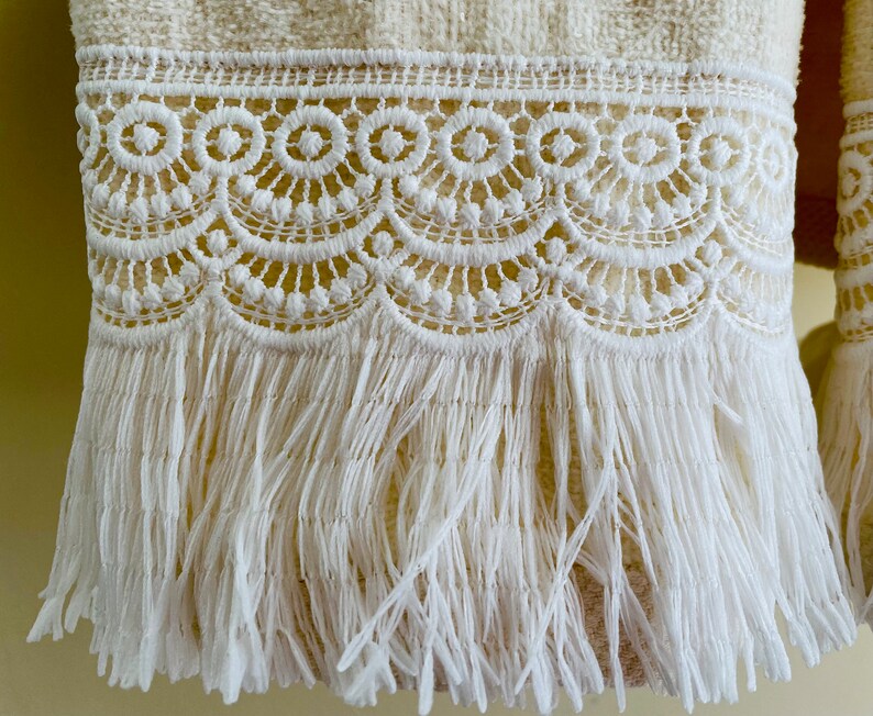 May include: A white towel with a white crocheted lace trim and fringe. The fringe is long and flowing.