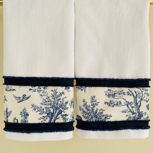 May include: Two white bath towels with a navy blue trim and a toile pattern. The pattern features blue and white trees, birds, and flowers.