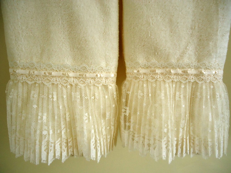May include: Two white towels with a lace trim. The lace is a delicate, off-white color and has a ruffled edge. The towels are soft and fluffy.