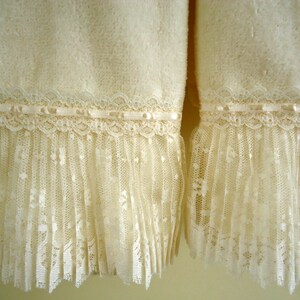 May include: Two white towels with lace trim. The towels have a fluffy texture and are decorated with a delicate lace trim.