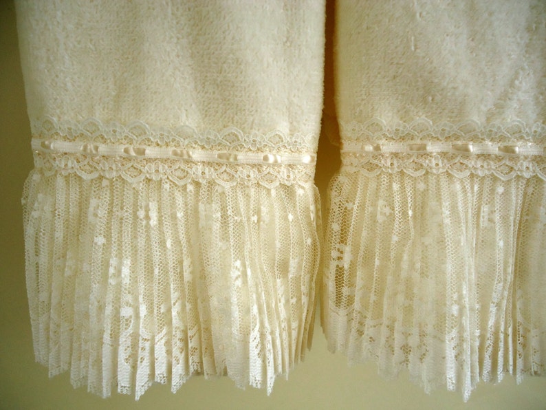 May include: Two white towels with lace trim. The towels have a fluffy texture and are decorated with a delicate lace trim.