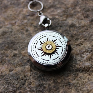 May include: A silver locket with a sun design and a .380 Auto bullet in the center. The locket has a silver chain attached.