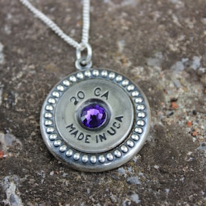 Puede incluir: Un collar de plata con un colgante redondo que presenta una piedra preciosa púrpura y el texto "20 GA MADE IN USA".