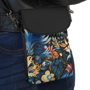 Puede incluir: Una bolsa de teléfono cruzada de cuero negro con un patrón floral. El patrón presenta colores azules, amarillos, rojos y verdes sobre un fondo negro.