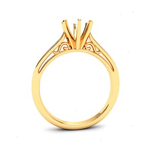 May include: A gold ring with a delicate, ornate design. The ring has a center setting for a stone, and the band is thin and delicate.