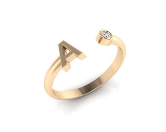 May include: A gold ring with a single diamond set in the band. The ring is shaped like the letter "A".