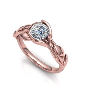 May include: A rose gold engagement ring with a round brilliant cut diamond set in a delicate, leaf-shaped design.