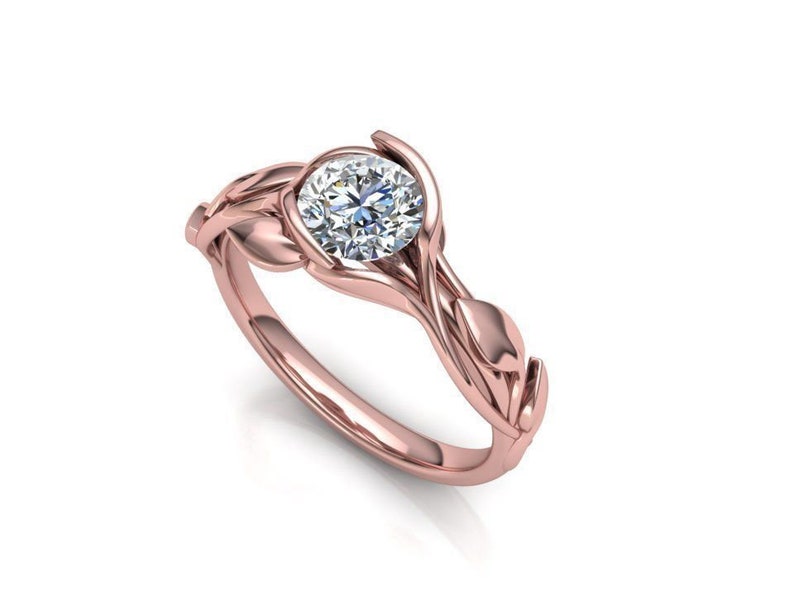 May include: A rose gold engagement ring with a round brilliant cut diamond set in a delicate, leaf-shaped design.