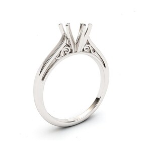 May include: A silver ring setting with a delicate, ornate design. The setting is designed to hold a center stone, with prongs to secure it in place.