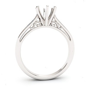May include: A silver ring setting with a delicate, ornate design. The setting has a three-prong head and a thin band.