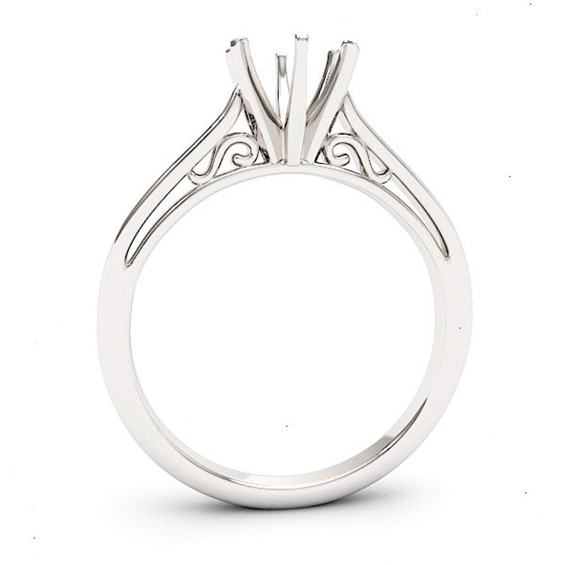 May include: A silver ring setting with a delicate, ornate design. The setting has a three-prong head and a thin band.