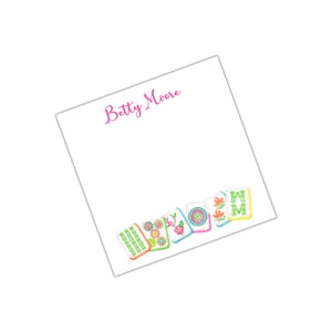 May include: White notepad with the name "Betty Moore" printed in pink at the top. The bottom edge of the notepad features a row of colourful mahjong tiles with various symbols and designs.