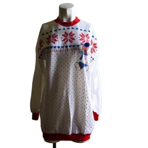 May include: White long-sleeved sweater with a red and blue snowflake pattern around the neck and a red trim around the bottom. A cartoon bear wearing a blue and red outfit is printed on the front of the sweater.
