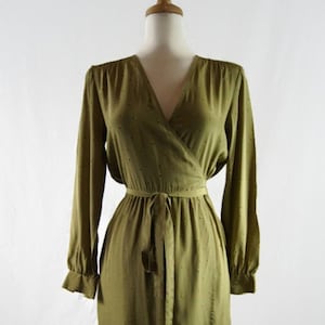 May include: A long-sleeved olive green wrap dress with a small white polka dot pattern. The dress has a V-neckline and a tie belt at the waist.