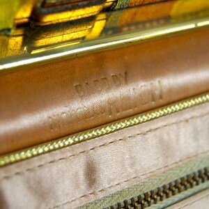Puede incluir: Primer plano del interior de un bolso vintage. El interior presenta un forro de sat&eacute;n marr&oacute;n claro con una cremallera y costuras doradas. Las palabras "MADE BY" y "MCGILL" est&aacute;n grabadas en el cuero. El cierre es dorado.