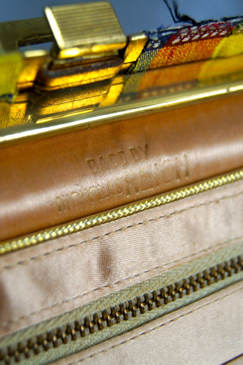 Puede incluir: Primer plano del interior de un bolso vintage. El interior presenta un forro de sat&eacute;n marr&oacute;n claro con una cremallera y costuras doradas. Las palabras "MADE BY" y "MCGILL" est&aacute;n grabadas en el cuero. El cierre es dorado.