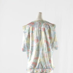 May include: A vintage blouse with a pastel floral pattern in pink, blue, yellow, and green. The blouse has short sleeves, a round neckline, and a gathered waist. The fabric appears to be lightweight and silky.