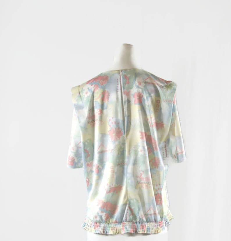 May include: A vintage blouse with a pastel floral pattern in pink, blue, yellow, and green. The blouse has short sleeves, a round neckline, and a gathered waist. The fabric appears to be lightweight and silky.