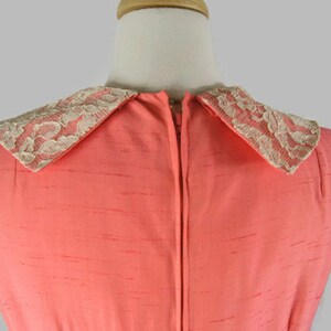 May include: A coral pink sleeveless dress with a white lace collar. The dress has a zipper down the back.