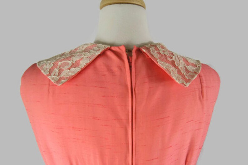 May include: A coral pink sleeveless dress with a white lace collar. The dress has a zipper down the back.