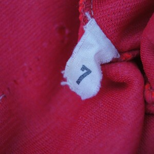 May include: Close-up of a red fabric tag with the number "7" printed on it.