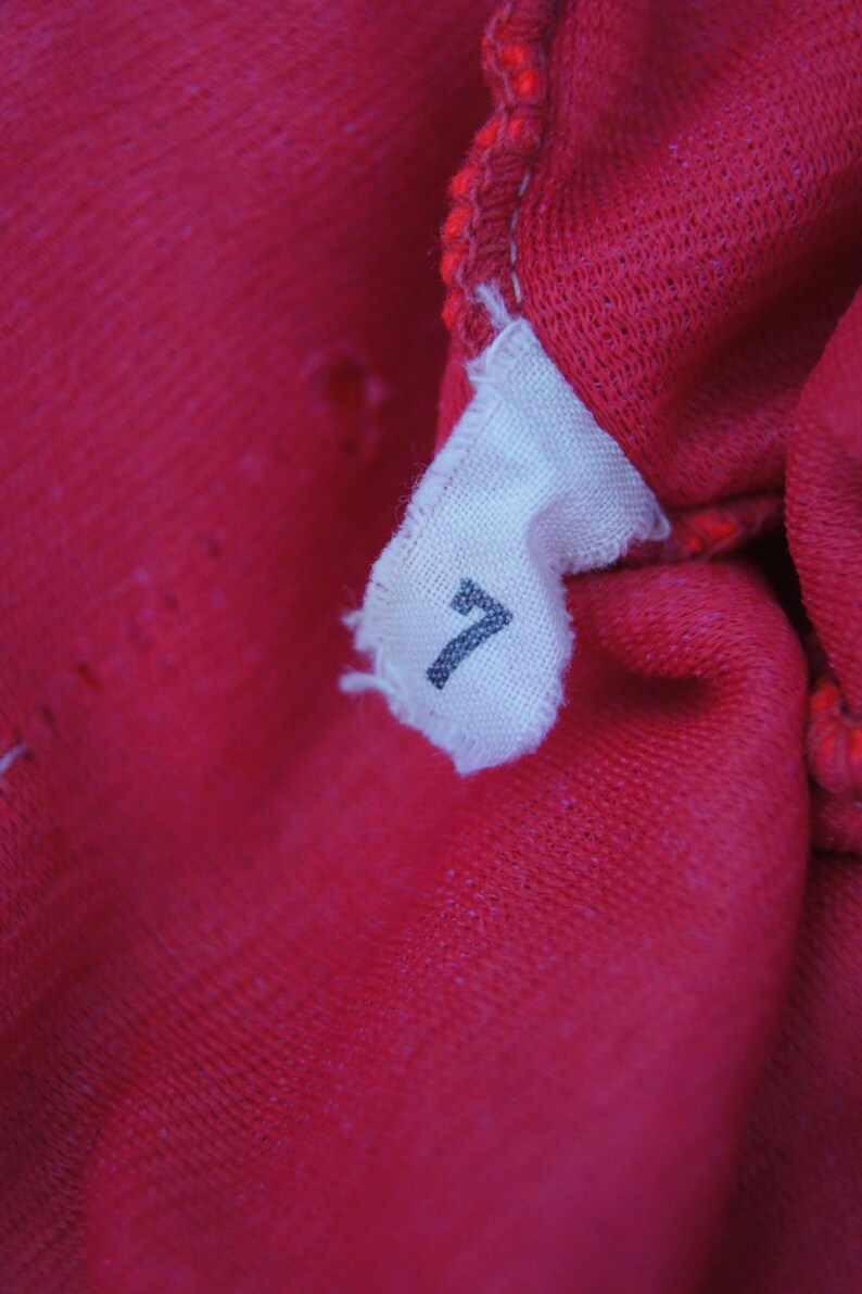 May include: Close-up of a red fabric tag with the number "7" printed on it.
