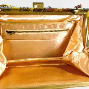 Puede incluir: Bolso vintage abierto con marco y cierre dorados. El interior presenta un forro de sat&eacute;n color melocot&oacute;n y un bolsillo con cremallera. El exterior es un colorido estampado de cuadros con tonos amarillos, naranjas y azules.