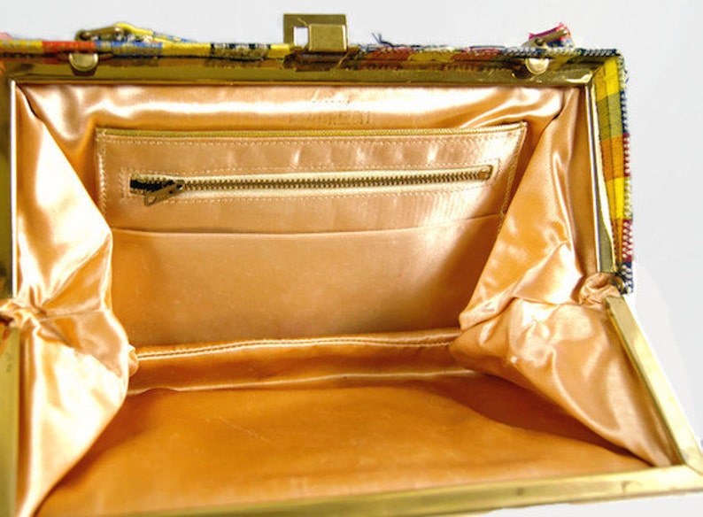 Puede incluir: Bolso vintage abierto con marco y cierre dorados. El interior presenta un forro de sat&eacute;n color melocot&oacute;n y un bolsillo con cremallera. El exterior es un colorido estampado de cuadros con tonos amarillos, naranjas y azules.