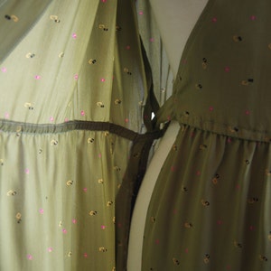 May include: A green, sheer dress with a small, repeating pattern of pink and gold shapes. The dress has a V-neckline and a tie at the waist.