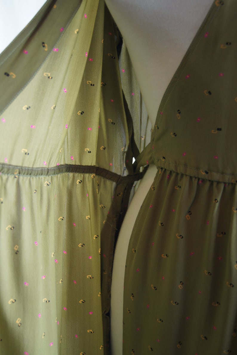 May include: A green, sheer dress with a small, repeating pattern of pink and gold shapes. The dress has a V-neckline and a tie at the waist.