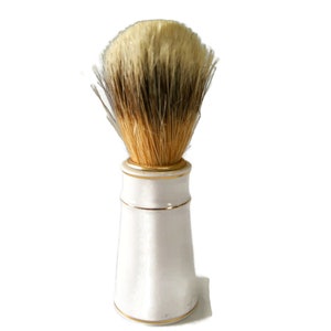 May include: A white ceramic shaving brush with a gold trim and a brown and white bristle brush head.