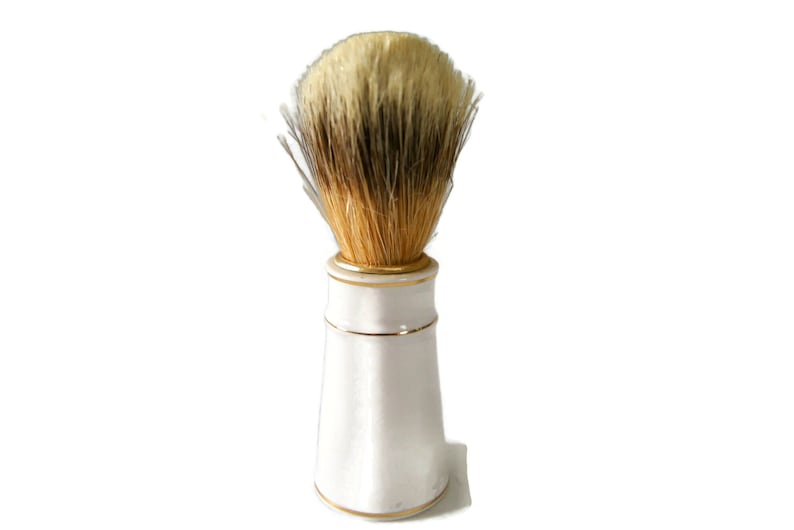 May include: A white ceramic shaving brush with a gold trim and a brown and white bristle brush head.