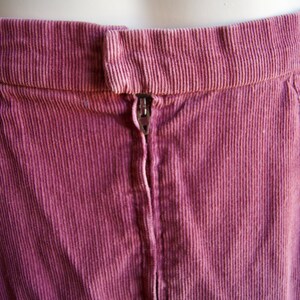 May include: A close-up of the back of a pink corduroy skirt with a zipper closure.