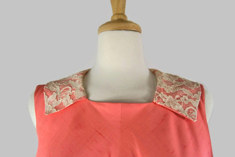 May include: A sleeveless coral dress with a white lace collar.