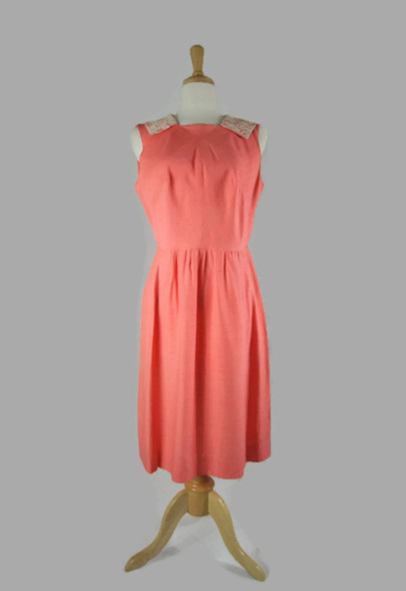 May include: A sleeveless coral pink dress with a white lace collar. The dress has a fitted bodice and a full skirt.