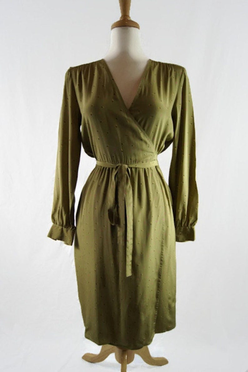 May include: A long-sleeved olive green wrap dress with a small white polka dot pattern. The dress has a V-neckline and a tie belt at the waist.