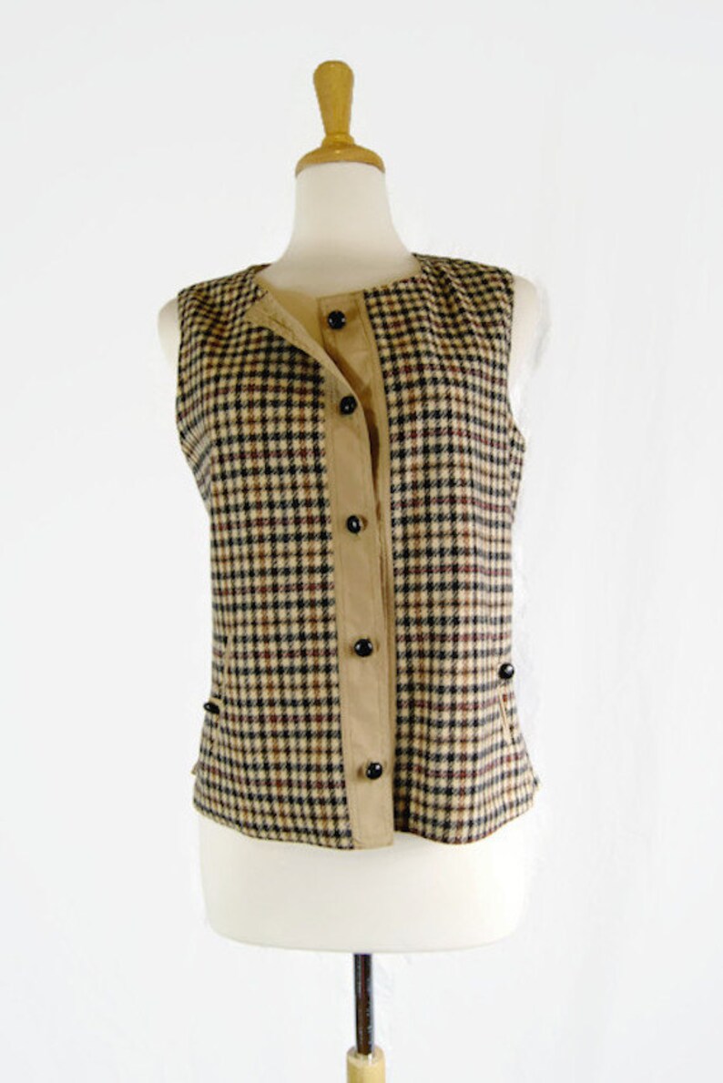May include: A sleeveless vest with a brown and black plaid pattern. The vest has a button-up front and a brown fabric lining.