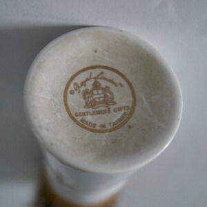 May include: Close-up of a white ceramic bottom of a vase with a gold logo that reads "Royal London, Gentlemen's Gifts, Made in Taiwan."